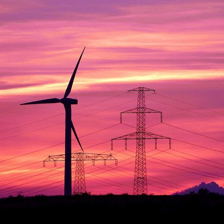 Windrad vor Strommasten im Sonnenuntergang