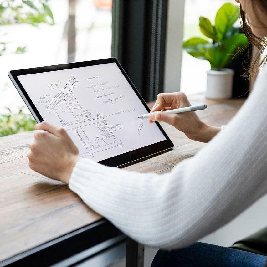 Architektin plant am Tablet und sitzt am Fenster mit Aussicht ins Grüne
