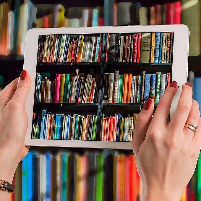 Frau fotografiert mit Tablet ein Bücherregal