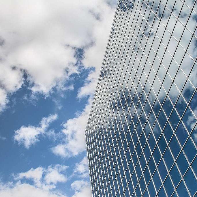 Wolken spiegeln sich in der Glasfassade eines Hochhauses